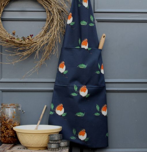 Robin on midnight blue apron hanging against a white stone wall and surrounded by baking equipment